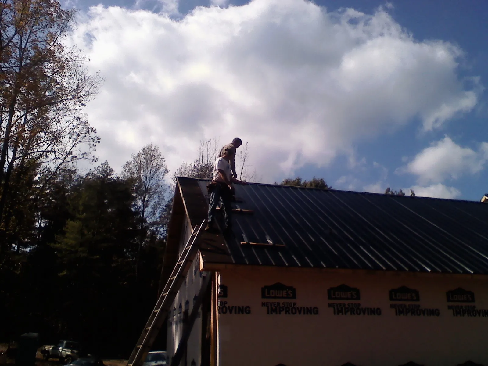 Roofer fastening dark metal panels high against a cloudy sky, from a Roof Inspection job in Bristol